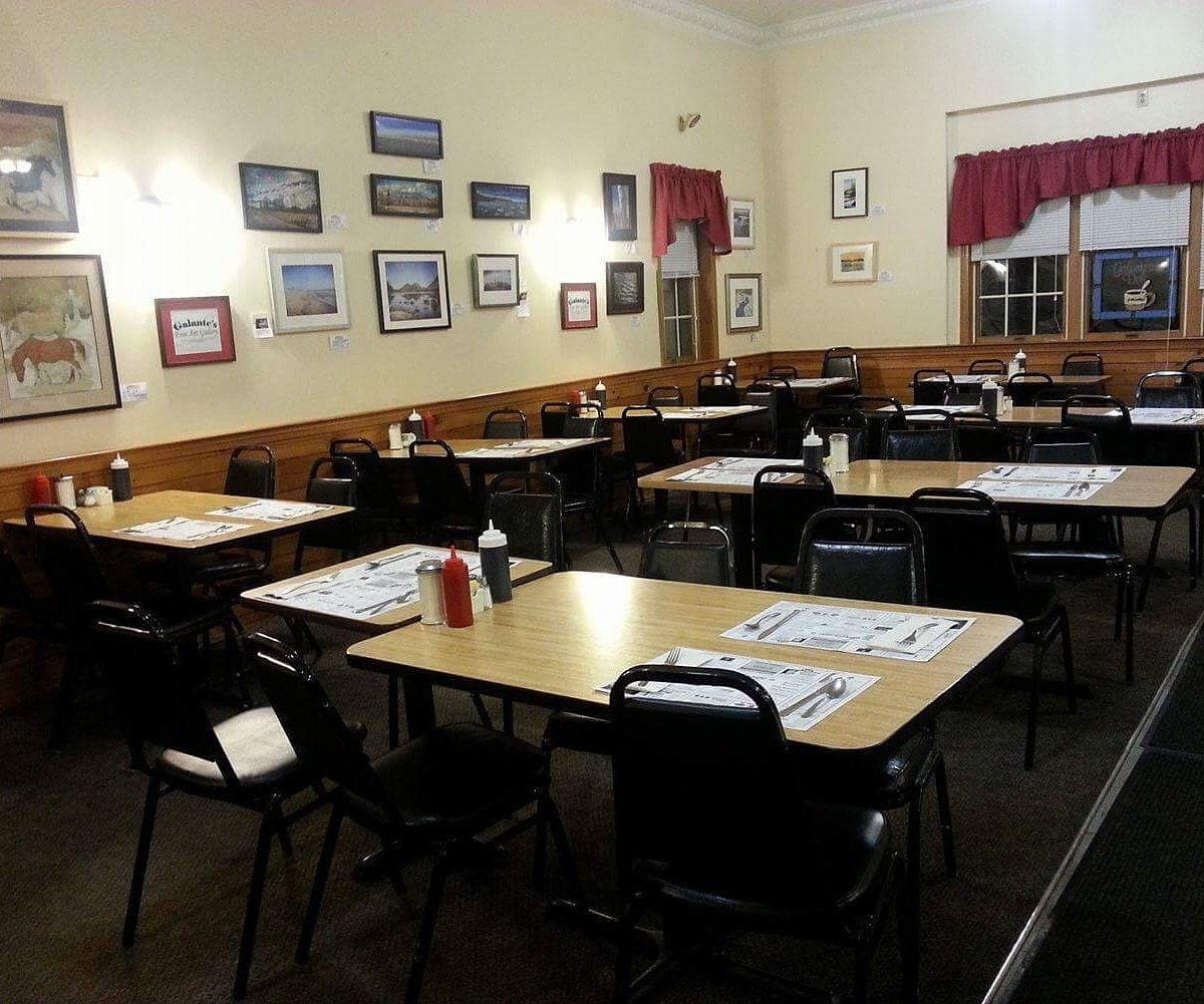 The dining room set for breakfast: wood-grain tables with paper placemats, black chairs, and cream walls hung with framed pictures.