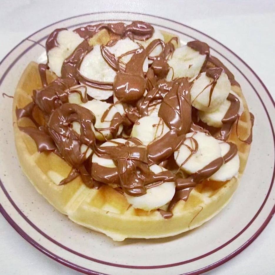 A Belgian waffle topped with sliced banana and Nutella.