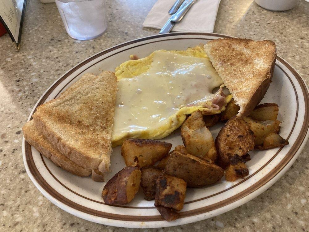 Two eggs scrambled with ham and melted cheese, with home fries and toast, on the counter.